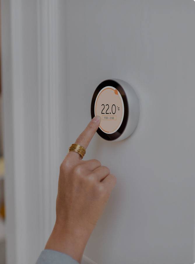 Una mujer pulsa en un termostato digital en una casa para regular la temperatura